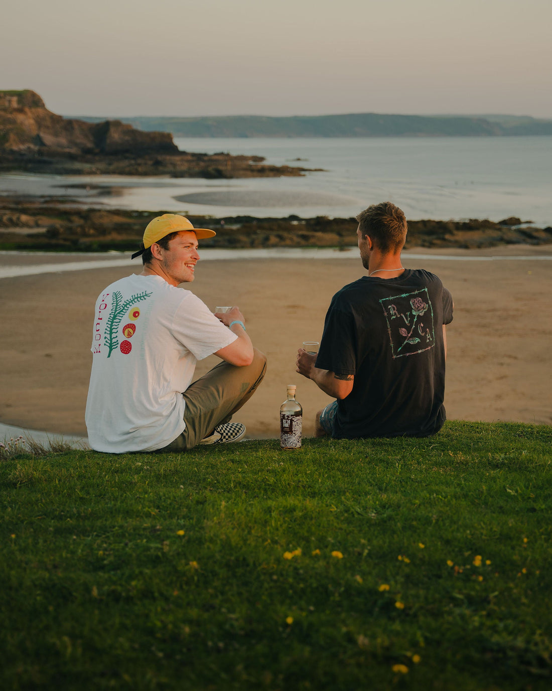 Two people overlooking a beach with drinks and a Rum Dhu bottle beside them